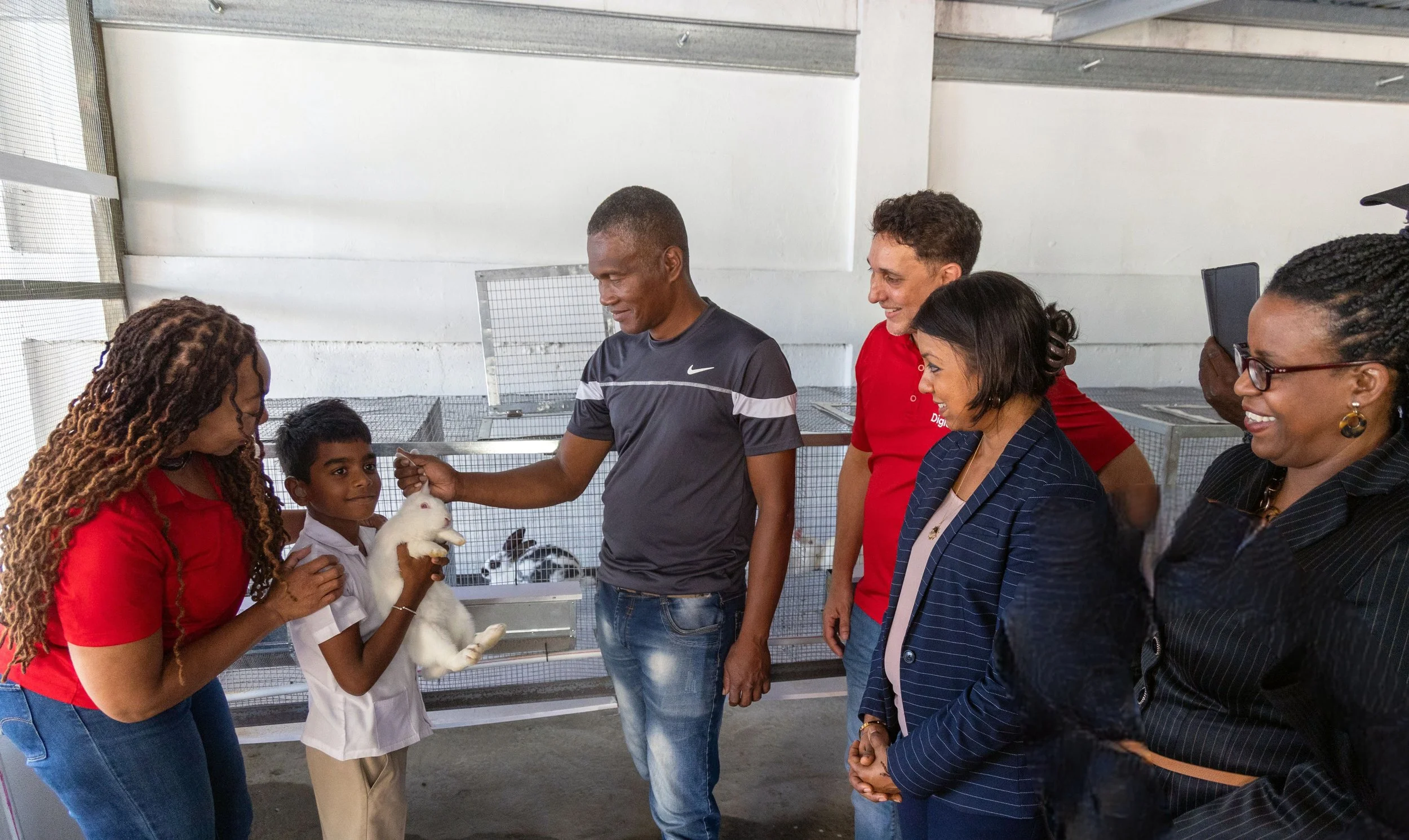  Student Amrit Williams gets comfortable holding one of the rabbits on the farm at the Tobago School for the Deaf, Speech and Language Impaired, bringing smiles to the faces of project stakeholders at the school’s agro-science project launch. From left to right: Penny Gomez, Chief Executive Officer, Digicel Foundation; Amrit Williams; Prior Alexander, Handyman, Tobago School for the Deaf, Speech and Language Impaired; Jason Matthews, General Manager-Digicel Plus, Digicel Trinidad and Tobago Limited; Desha Clifford, Chairperson, Digicel Foundation; Ann Second, Technical Advisor, Division of Education, Research and Technology.  