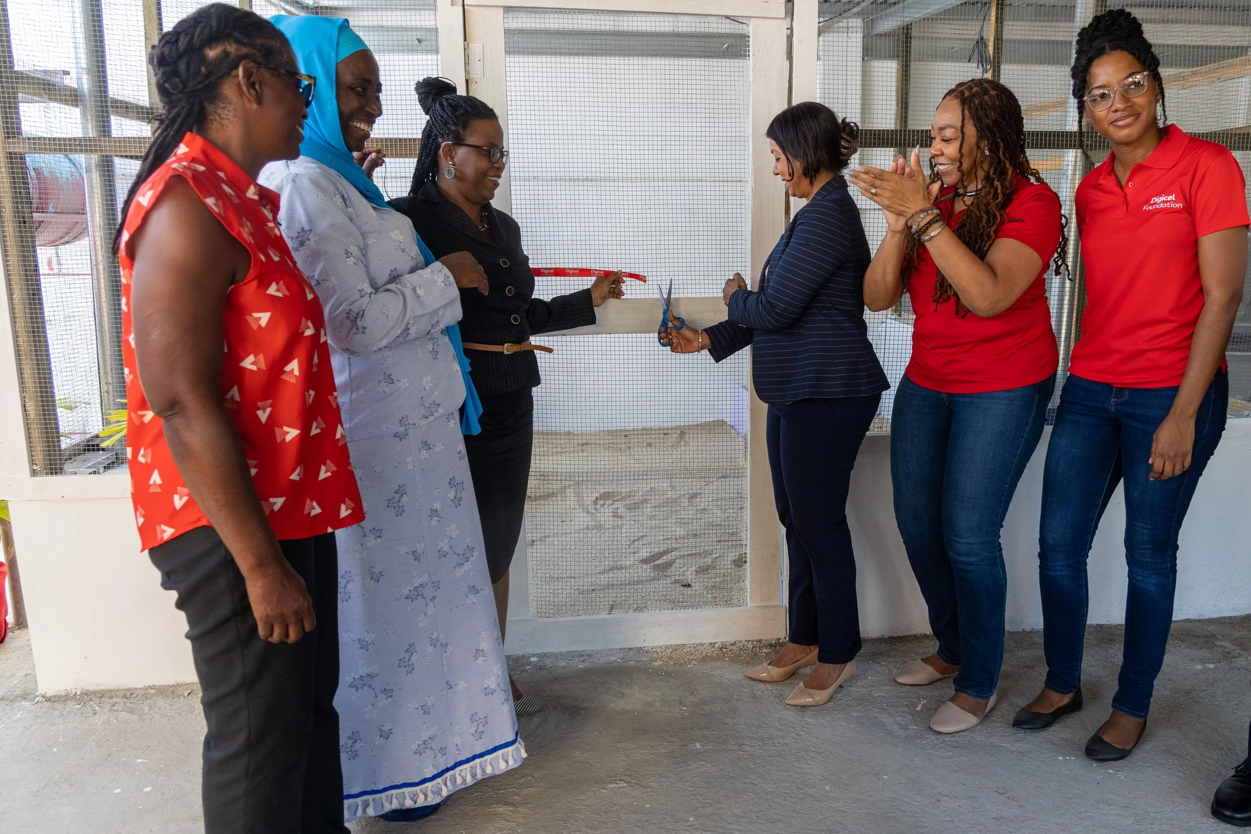  Digicel Foundation’s Chairperson Desha Clifford (centre right) cuts the ribbon on a chicken pen, launching the Tobago School for the Deaf, Speech and Language Impaired’s agro-science project to a round of applause from the Foundation’s CEO Penny Gomez. Also present, from left to right, are Olive James, Secretary, Tobago Agricultural Society; Cordella Pantin, Principal, Tobago School for the Deaf, Speech and Language Impaired; and Ann Second, Technical Advisor, Division of Education, Research and Technology; and Misha Jackman, Finance Accountant of Digicel Foundation.      