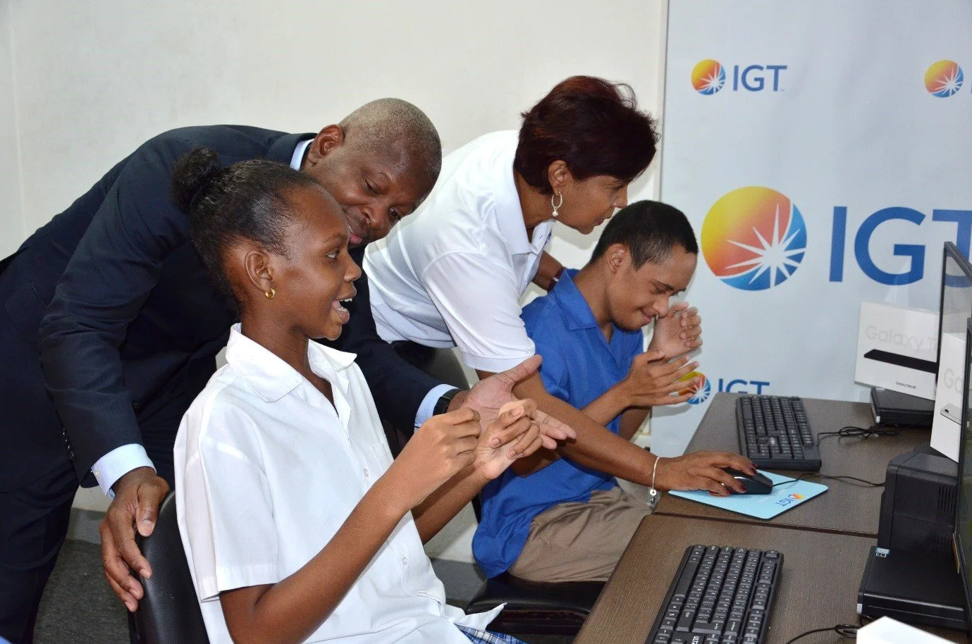 Dexter W. Thomas, IGT General Manager Trinidad & Tobago, and Shavindra Tewarie-Singh, IGT People & Transformation Regional Senior Manager for the Caribbean, assist these eager to learn students using the desktop computers donated to the Immortelle Centre through IGT’s After School Advantage programme.