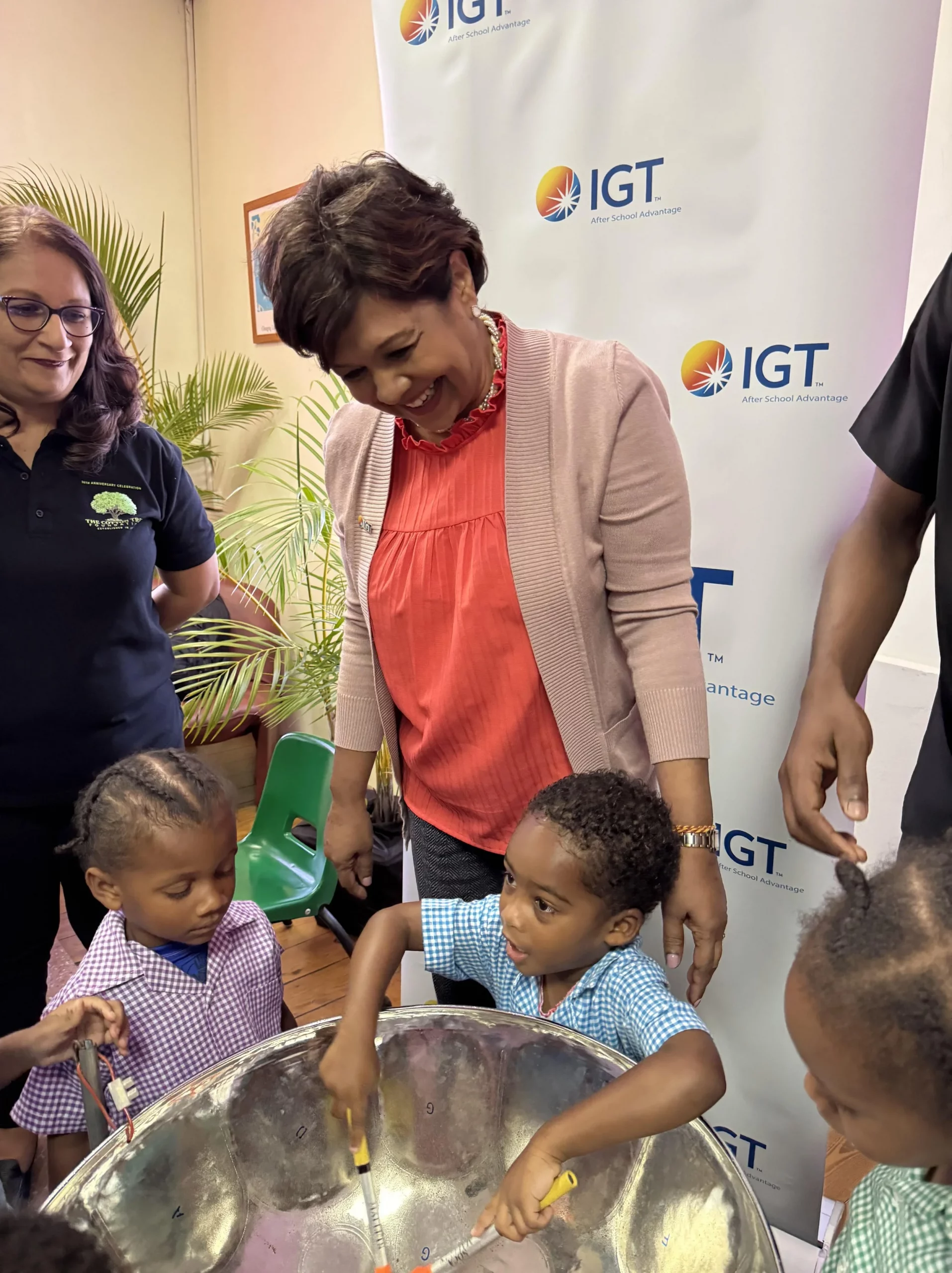  Preschool pan enthusiasts take turns on the steelpan under the watchful gaze of IGT P&T Regional Senior Manager for the Caribbean, Shavindra Tewarie-Singh, and Cotton Tree Foundation Executive Director Sita Persad (on the left). 