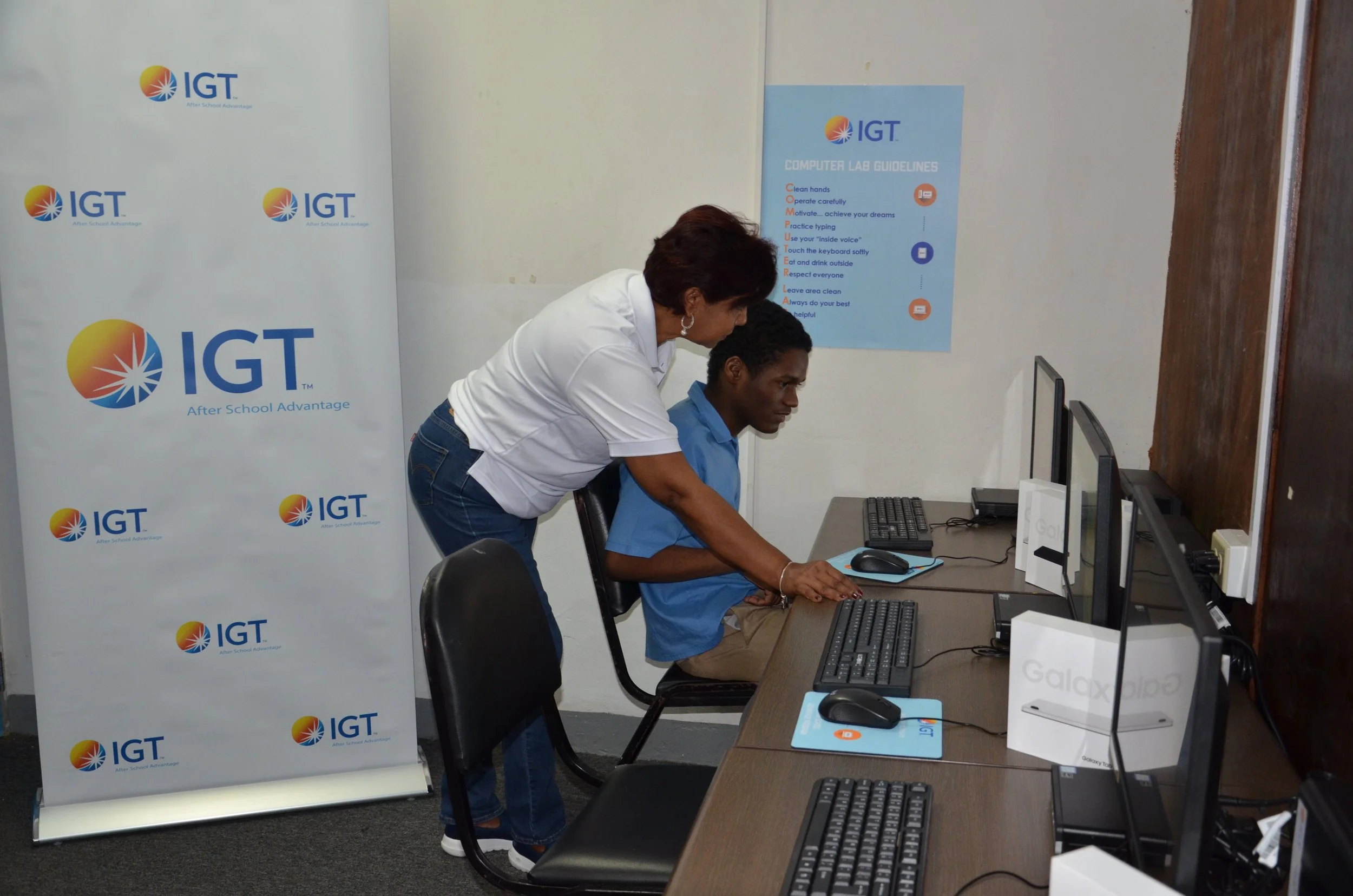 Shavindra Tewarie-Singh, IGT Senior Regional Human Resources Manager, Caribbean, assists a student using the newly installed desktop computer donated by IGT to the Immortelle Centre.
