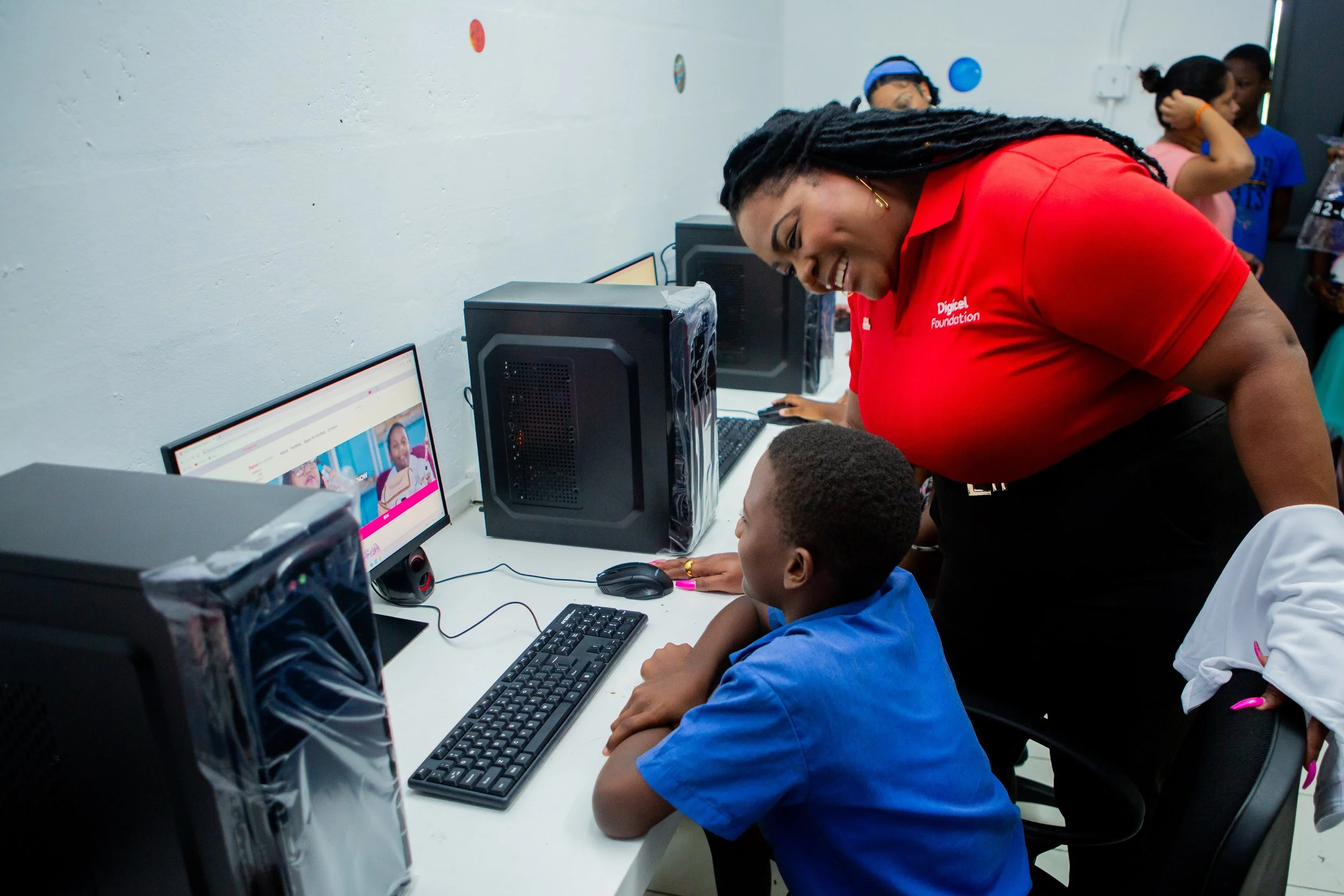 La Toya Gopaul, Digicel Foundation Director, looks on as this youngster gets comfortable in the Dass Trace Youth Empowerment Centre computer lab.