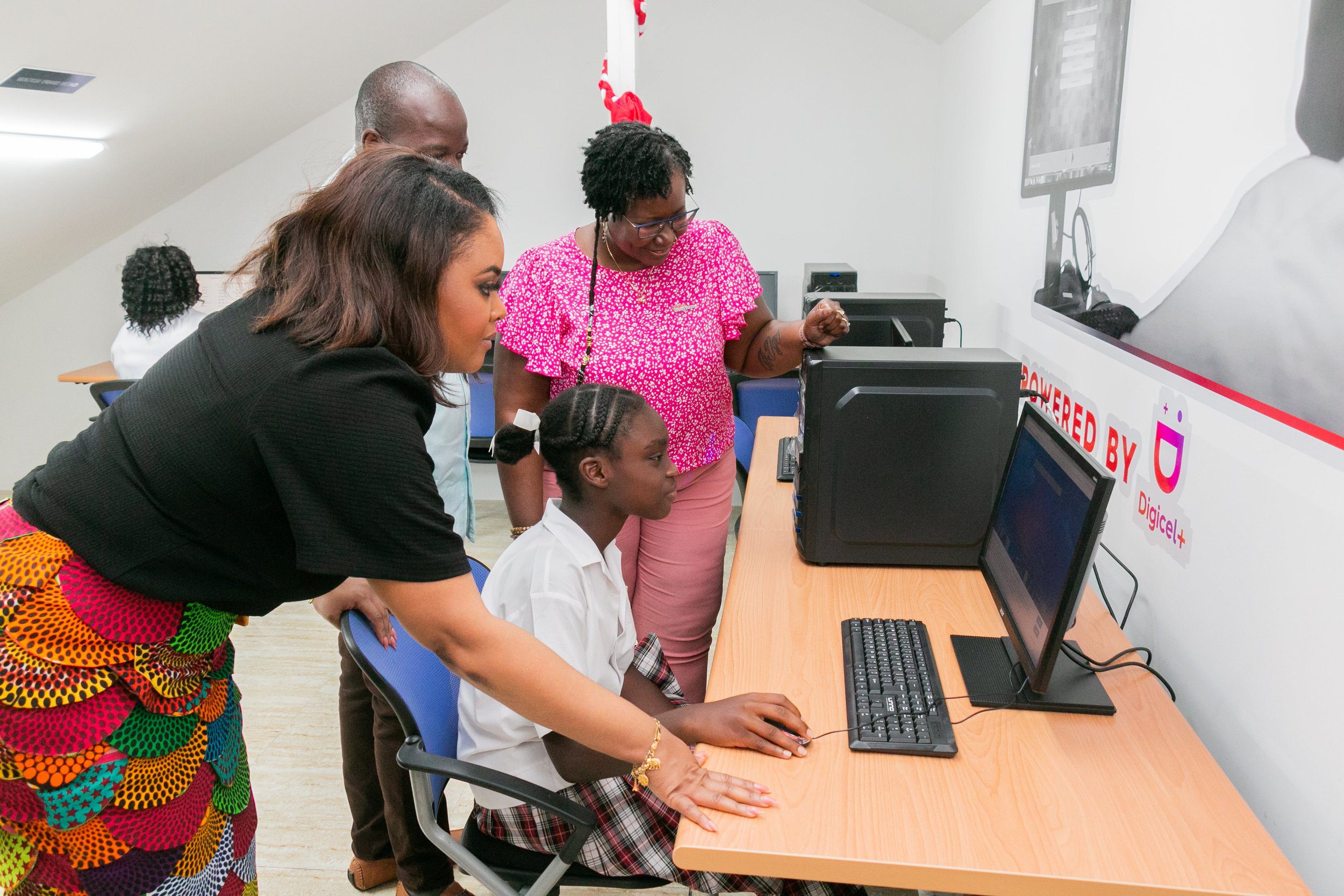 (L-R): Minister of Sport and Community Development Shamfa Cudjoe-Lewis; Manager of the Tobago Pan-Thers Brian Thomas; and Digicel Foundation Board Director Georgina Peterkin support a student using a desktop computer at the Tobago Pan-Thers Panyard Technology in Education Centre. 