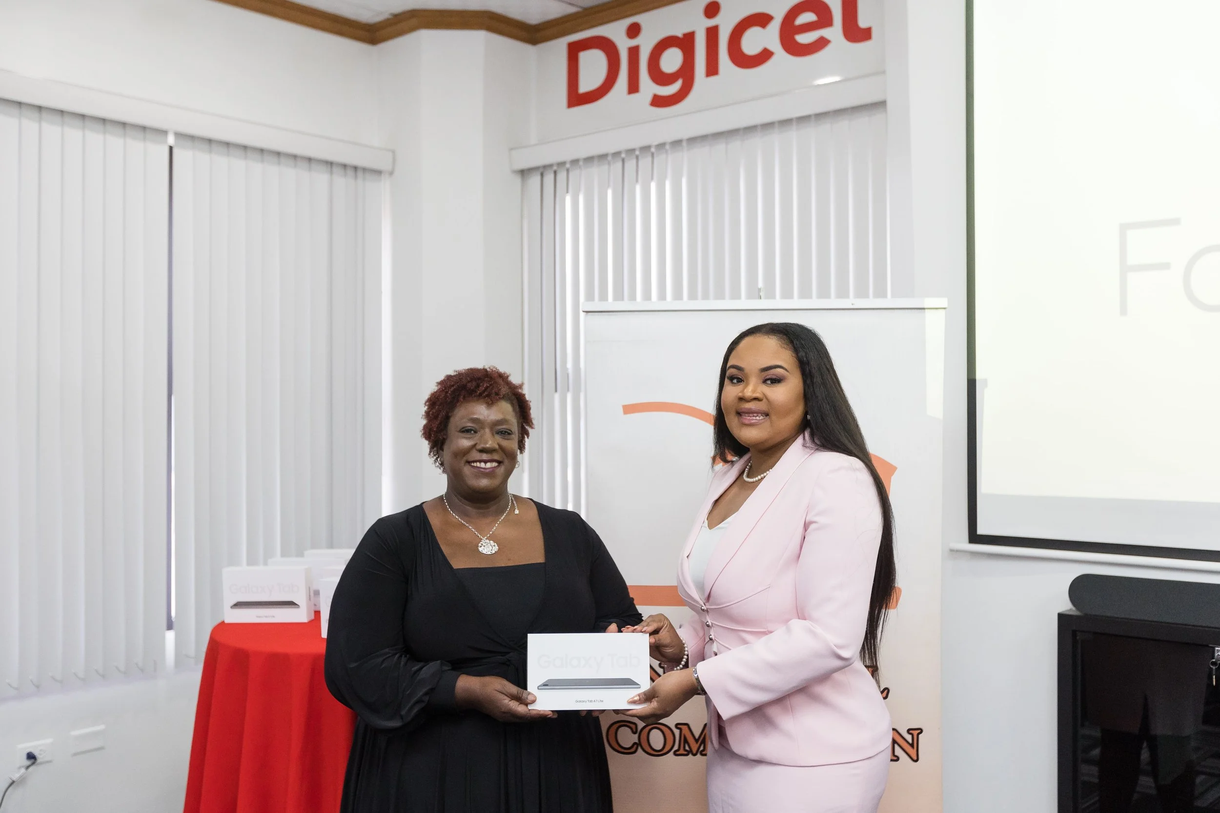 (L-R) Digicel Foundation Board member Laura Dowrich-Phillip presenting to the Hon. Shamfa Cudjoe, Minister of Sport and Community Development one of the Samsung Galaxy A7 Tablets.