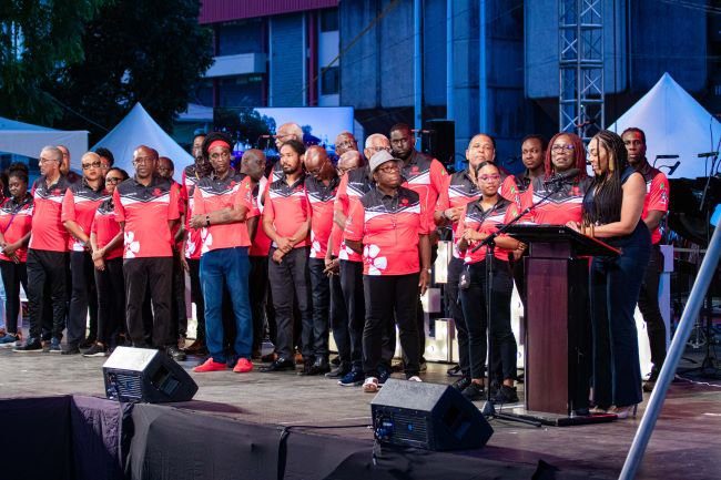  Members of PanTrinbago join   Digicel Foundation CEO Penny Gomez (at the podium) on stage during the World Steelpan Day Celebrations on 11 August 2023, Woodford Square, to announce their partnership to commission eight Technology in Education (TIE) Centres at panyards.  