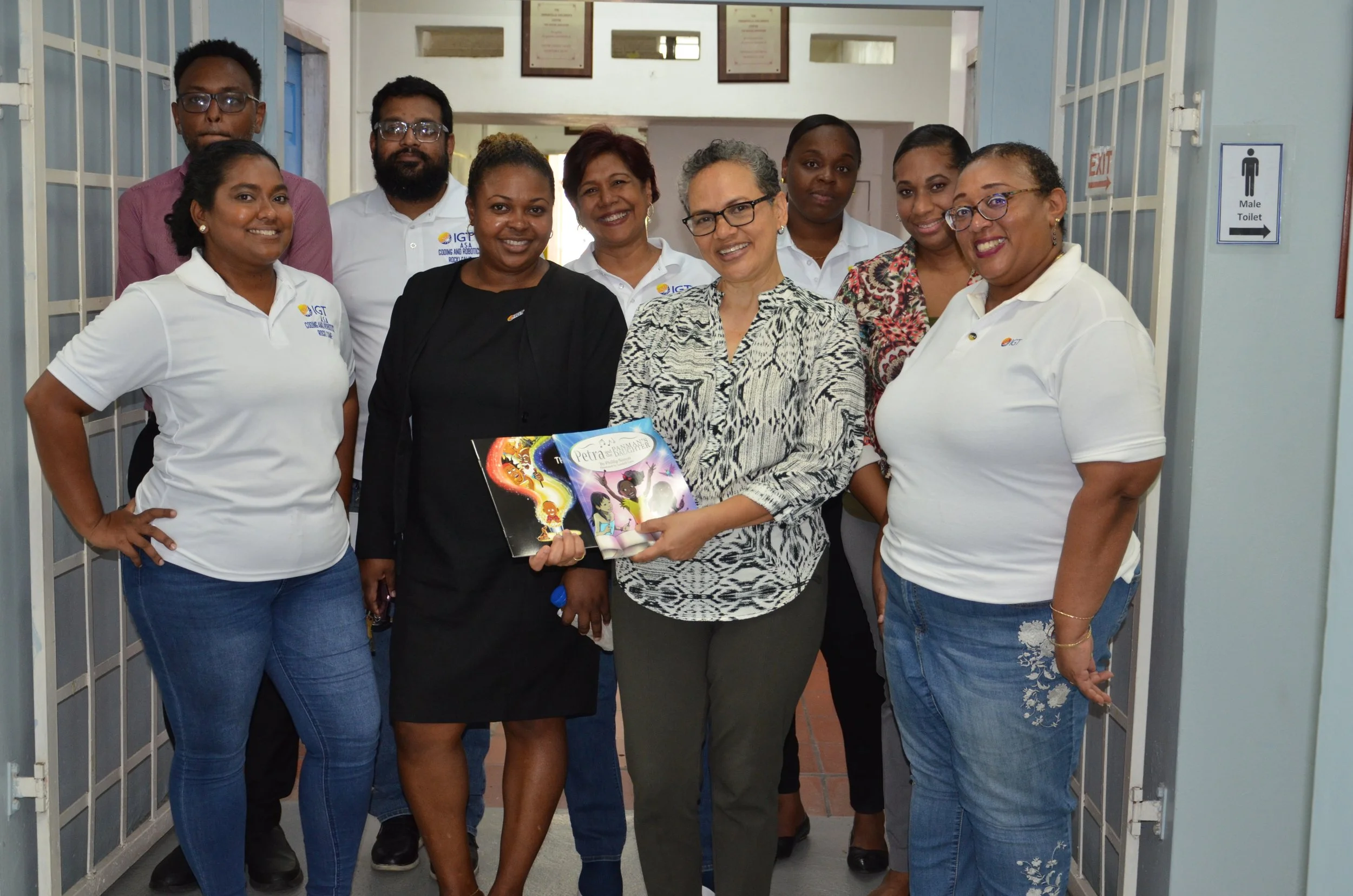 : Some of IGT’s volunteer team stand with Ms. Gittens, Principal of Immortelle Centre for Special Needs, as she displays copies of the local books donated to the Centre’s library following the storytelling activities led at Immortelle by IGT for the company’s Global Giving Month activities on 24 May.