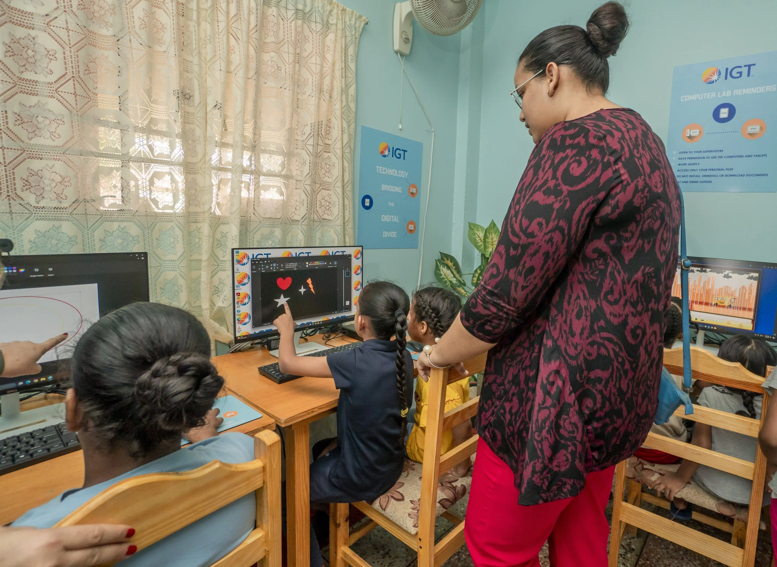 Amica’s assistant administrator, Marie Louise Belmare Singh, supervises the girls while they explore educational software on the new computers, courtesy IGT, on July 5th.