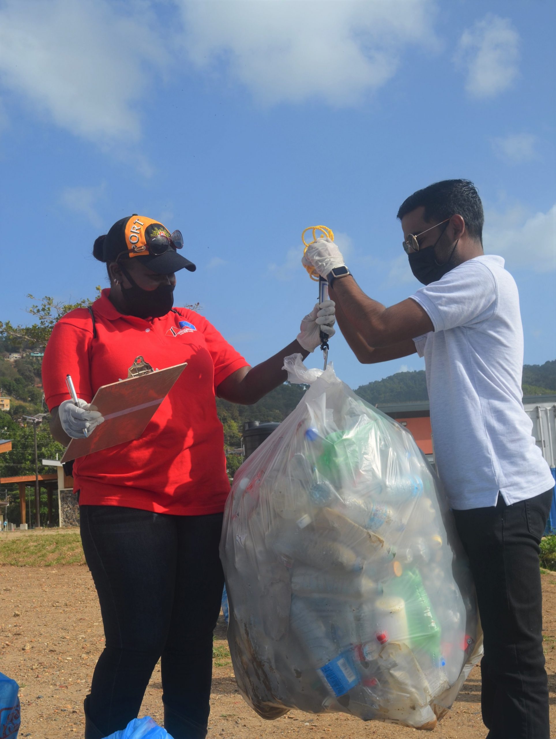 (L-R) Greta Joy Mc Kenzie, Senior Corporate Communications Officer, Communications Unit- Ministry of Planning and Development and Kevin Bhajan, Environmental Policy Analyst from the Ministry of Planning and Development Environmental Policy & Planning Division weigh a bag filled with plastic waste collected during the coastal clean-up exercise at the Carenage Fishing Centre.