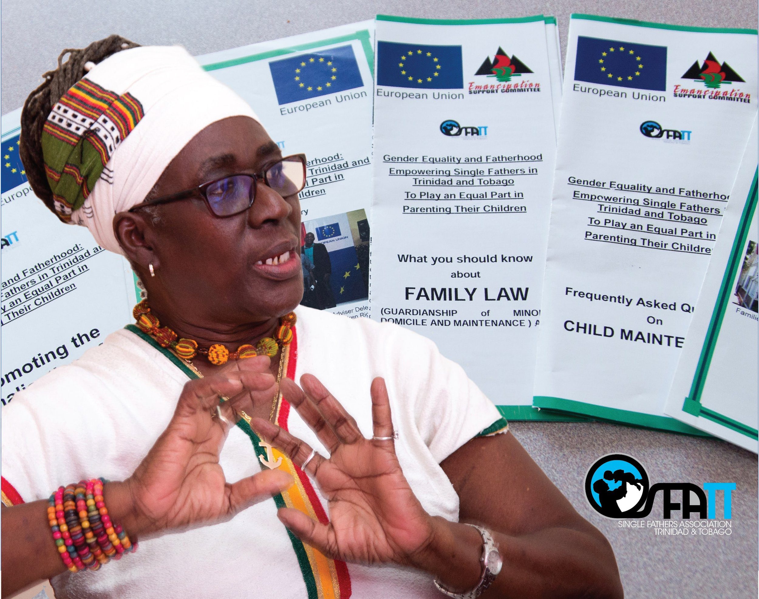 Executive Director of the Emancipation Support Committee Ms. Zakiya Naila Uzoma-Wadada against a backdrop of material published under the project to support the Single Fathers Association of Trinidad and Tobago (SFATT).
