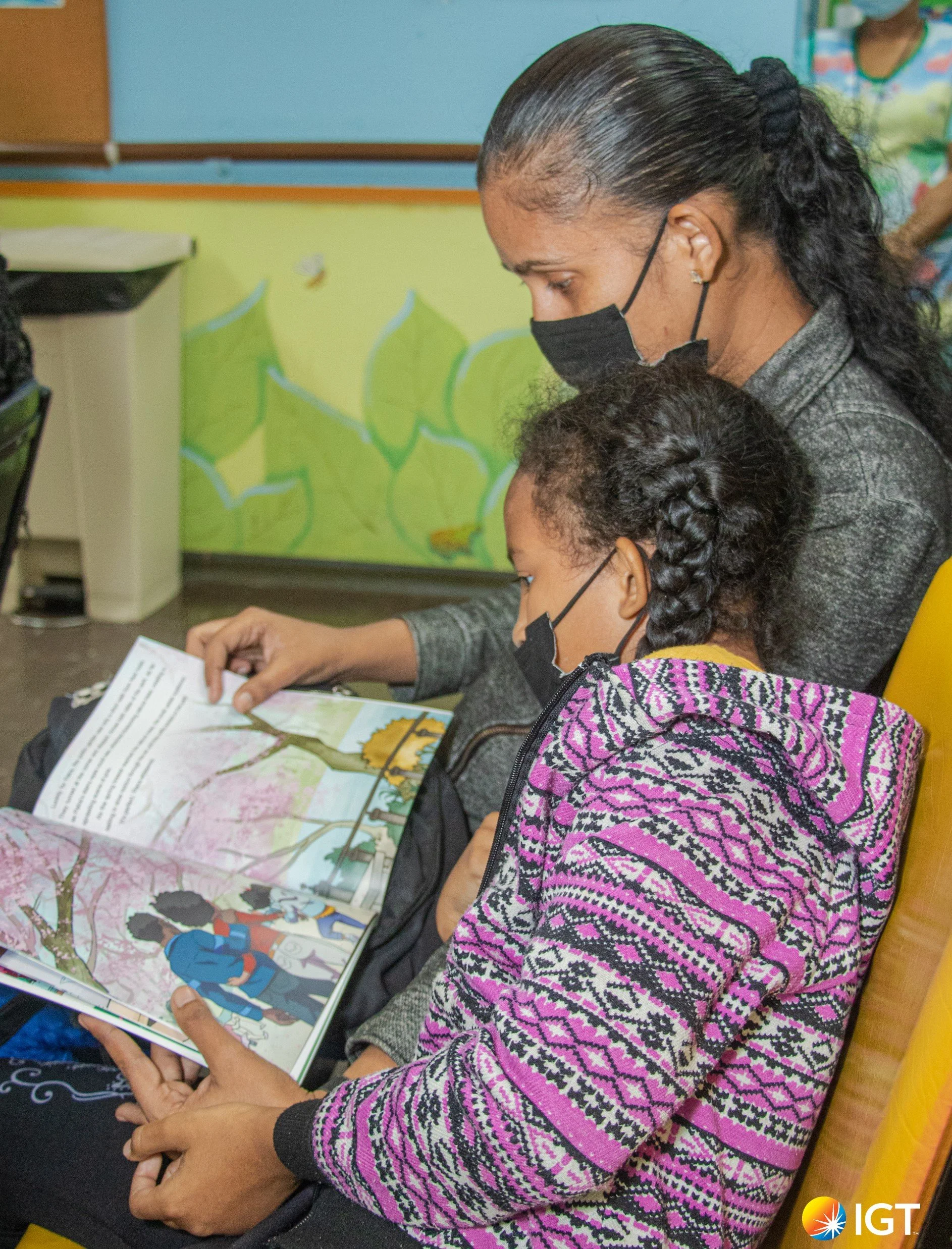 Kiara, a patient of the pediatric oncology clinic, enjoys a comforting moment with her mum reading together from the local children’s book, Petra and the Poui, to pass the time during the long wait for her appointment.