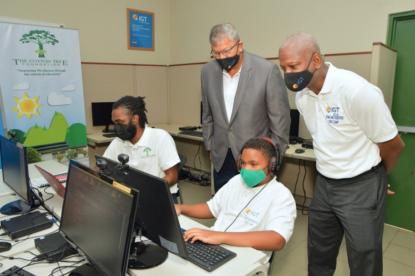 (L-R): Camp supervisor Isaiah Alexander, alongside IGT Country Manager Mr. Roger Bolai and Deputy Country Manager Dexter W. Thomas, oversees the progress of a student during the second staging of IGT Coding and Robotics Rock! Camp at the Cotton Tree Foundation.